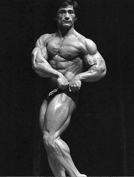 Danny Padilla twisting side chest pose on stage in black and white