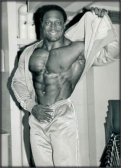 Lee Haney backstage pulling off his sweatshirt to reveal hoe ripped he was