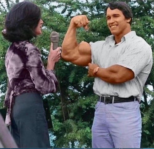 Arnold rolling up his sleeve to flex for a reporter
