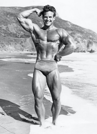 Steve Reeves flexing his biceps on a beach