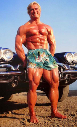 Tom Platz with huge quads in shorts at the beach in front of a Corvette