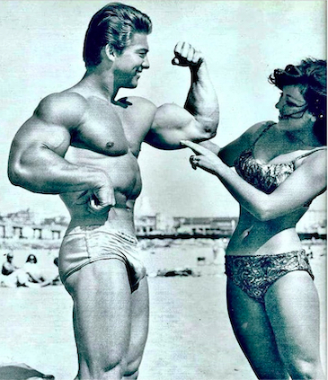 Larry Scott at the beach flexing his biceps for a girl