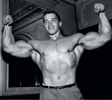 Young Arnold in a double biceps pose and wearing slacks