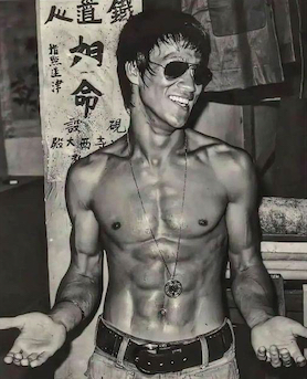 Bruce Lee in sunglasses with no shirt looking ripped