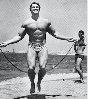 Arnold using a jump rope at the beach with a girl watching him
